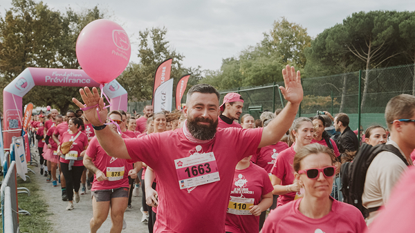 Homme habillé en rose souriant, les bras en l'air qui court