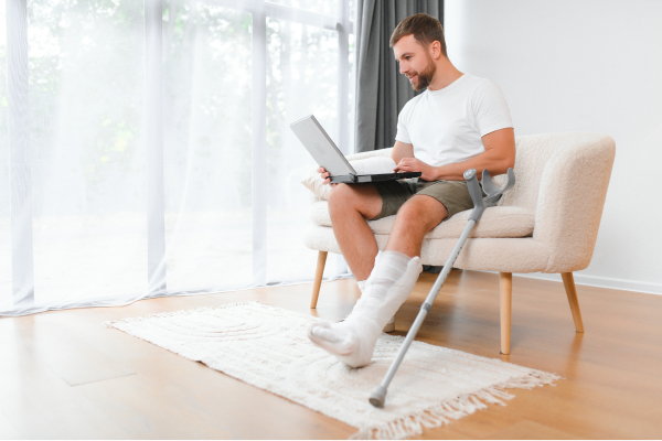 Homme avec un plâtre à la jambe assit qui utilise un ordinateur