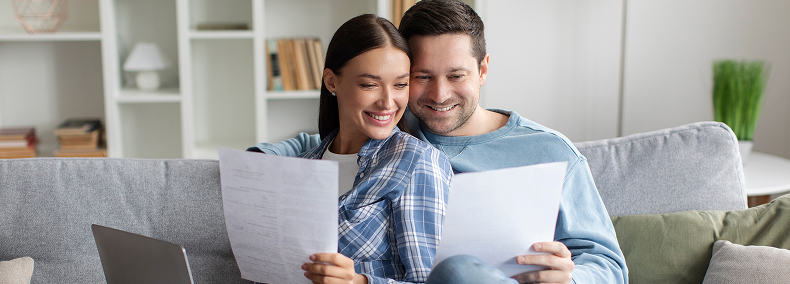 Couple souriant dans un canapé lisant des documents