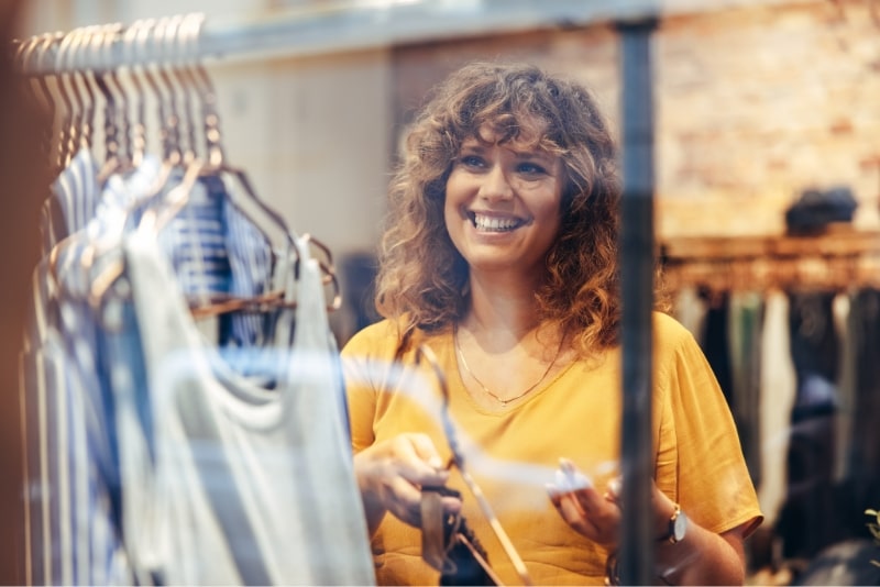 Femme souriante au t-shirt jaune faisant des achats dans une boutique de vêtements