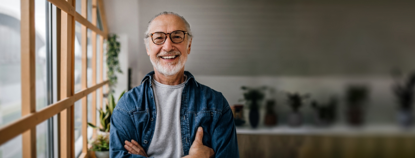 senior souriant avec des lunettes et les bras croises